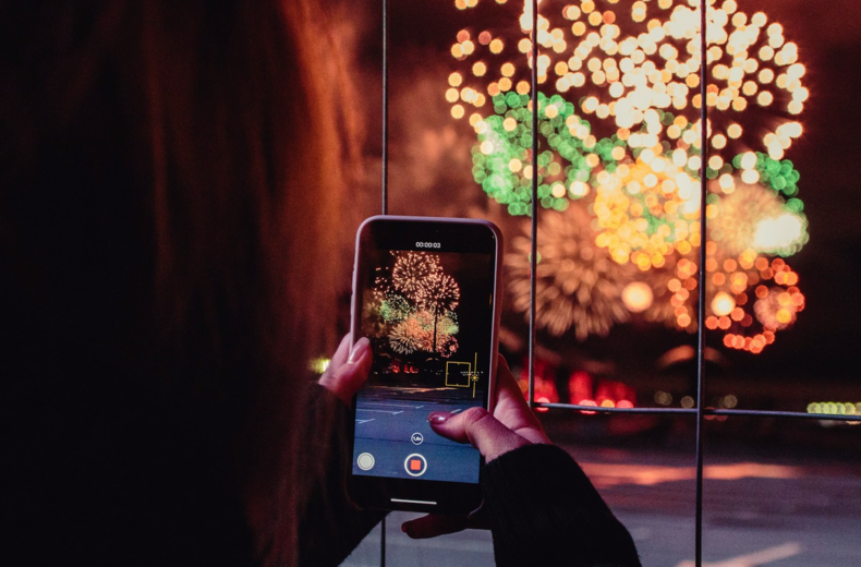 A person captures a photo of colorful fireworks lighting up the night sky.