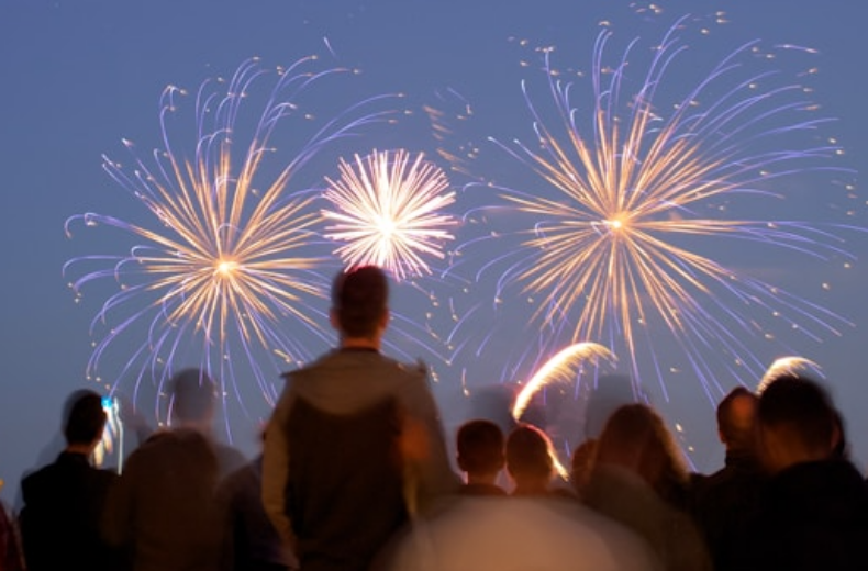 A crowd of people gazes up at colorful fireworks display illuminating the night sky.